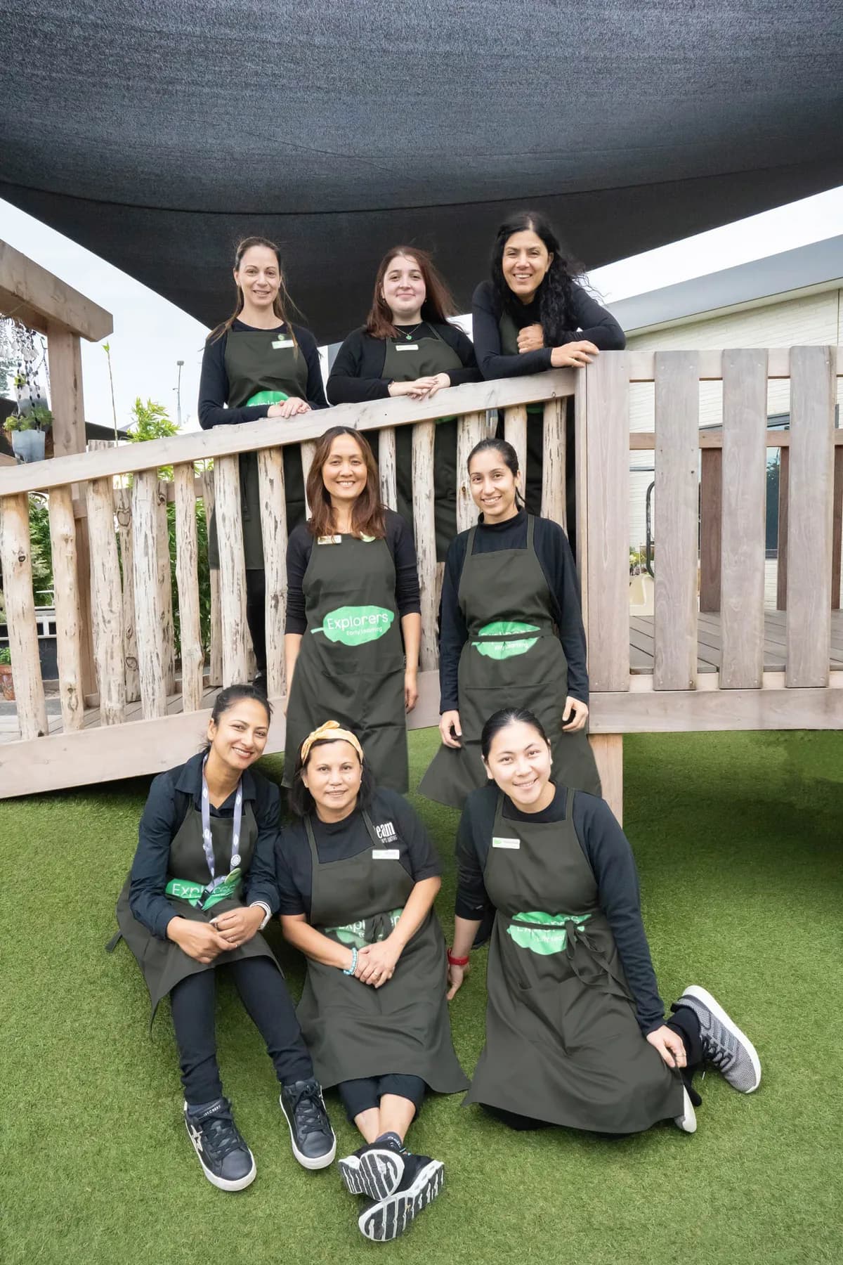 A group of smiling Explorers educators in black uniforms and green Explorers aprons