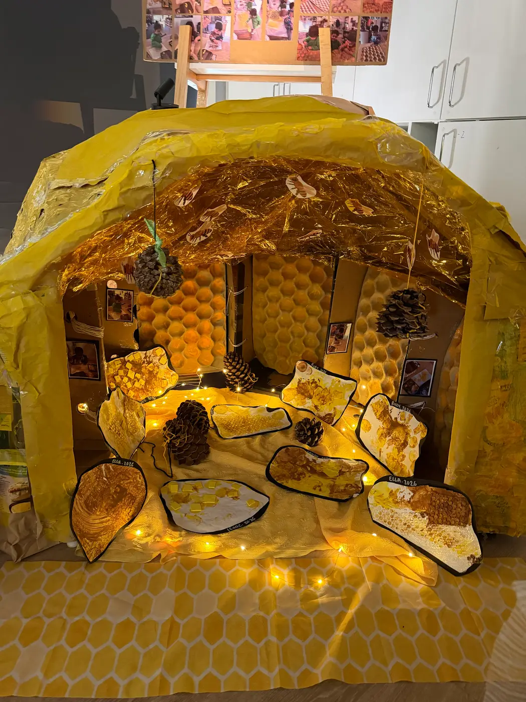 A golden honeycomb cave built for an art exhibition, with children’s artwork and pinecones inside