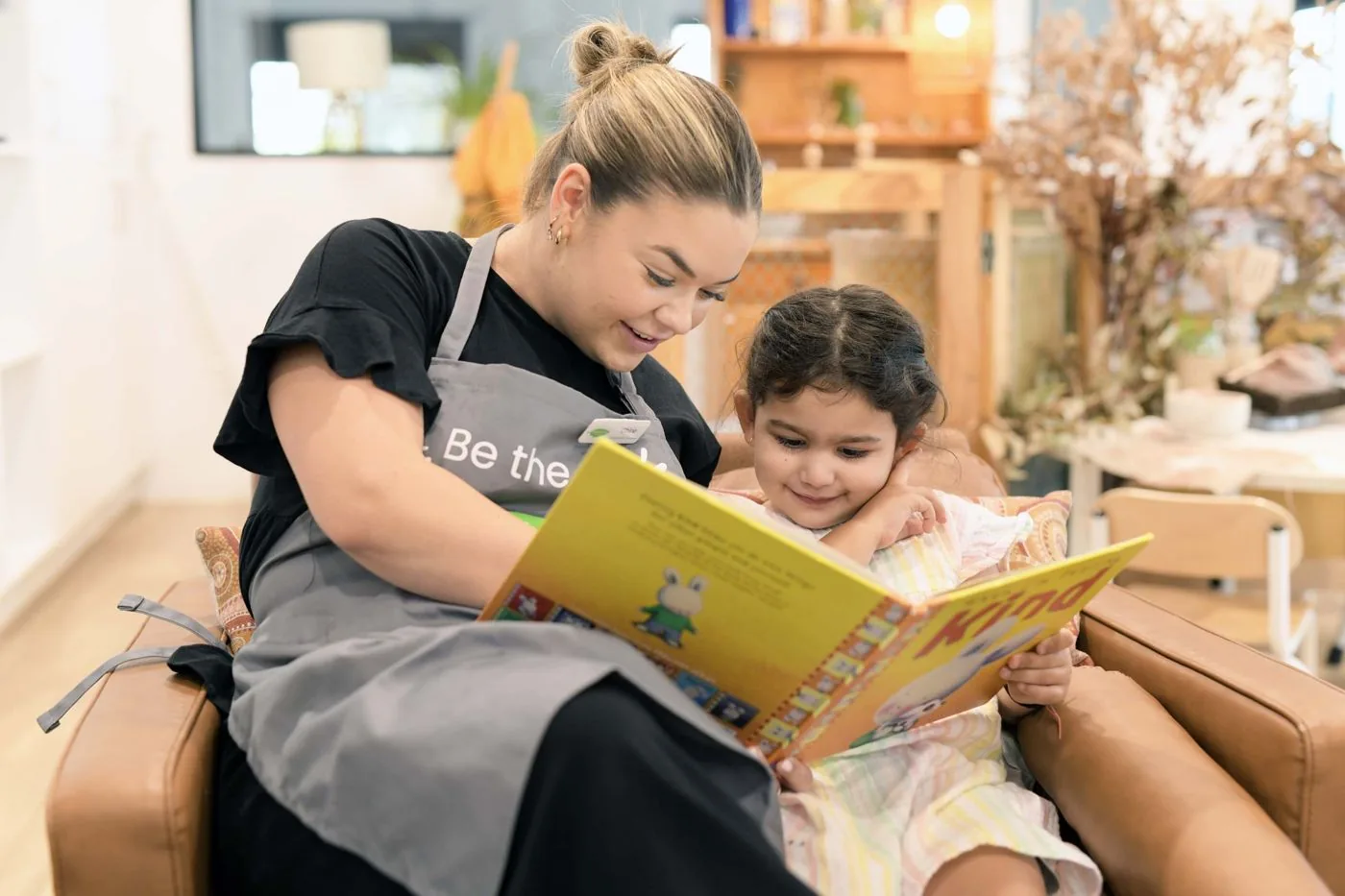 An educator reading a picture book with a young child in an armchair