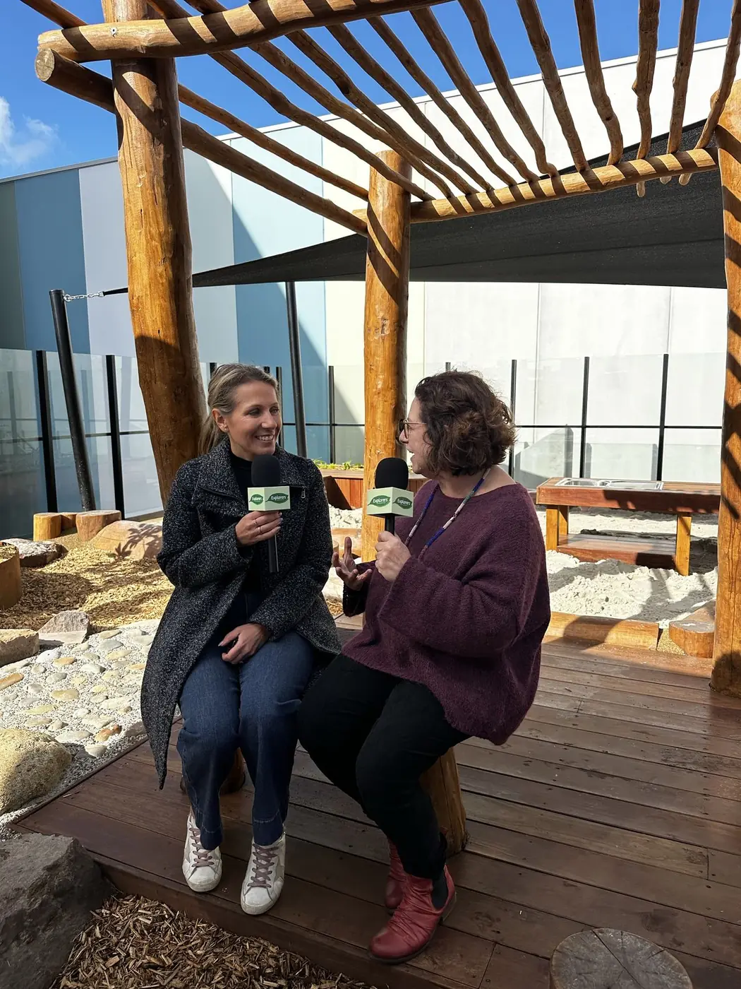 Two Explorers team members recording an interview under the timber pergola in the Armstrong Creek outdoor space