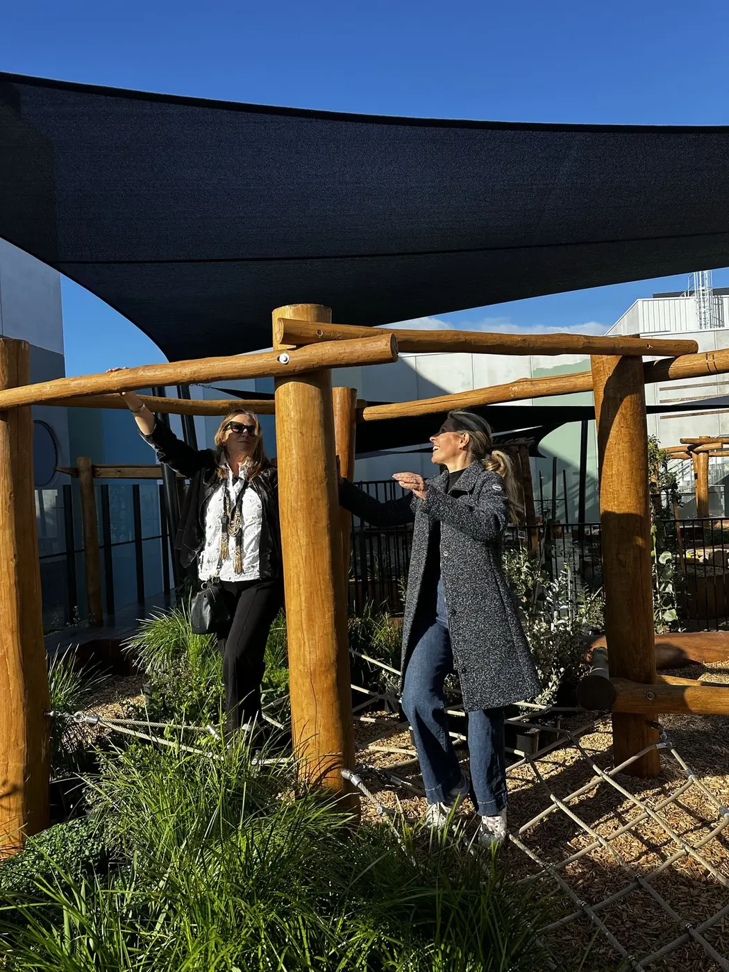 Two Explorers team members in the Armstrong Creek nature play space, one pointing out the timber climbing structure